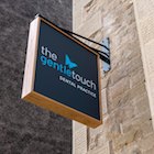 A grey hanging sign with oak frame and The Gentle Touch blue and white logo